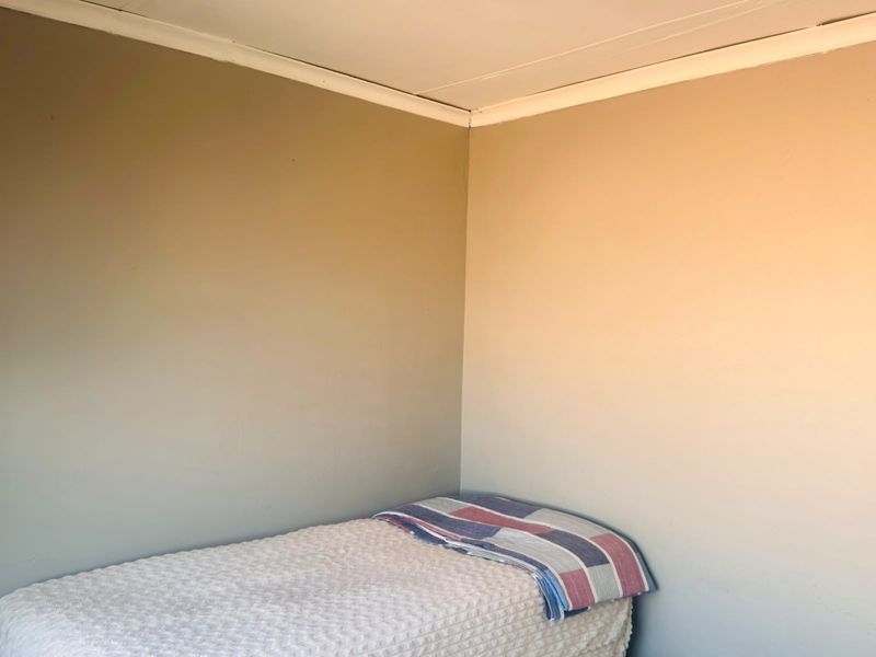 A simple, neutral-toned bedroom corner featuring basic wall finishes and ceiling cornicing.