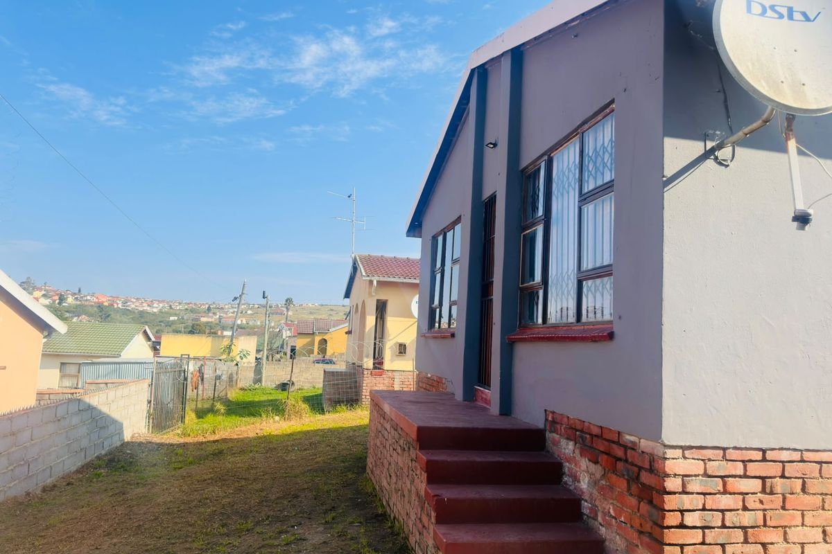 Rear exterior view of the house featuring brick steps, security bars on windows, and a satellite dish, set within a fenced residential plot.