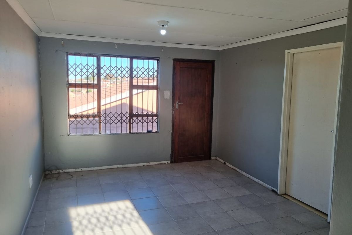An empty bedroom featuring tiled flooring, a security gate on the window, and a wooden door, offering a blank canvas for renovation.