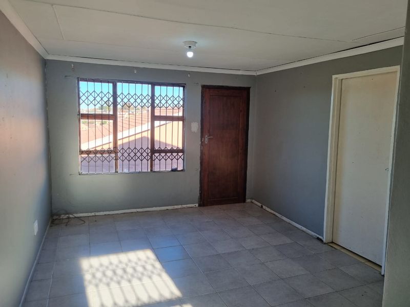An empty bedroom featuring tiled flooring, a security gate on the window, and a wooden door, offering a blank canvas for renovation.