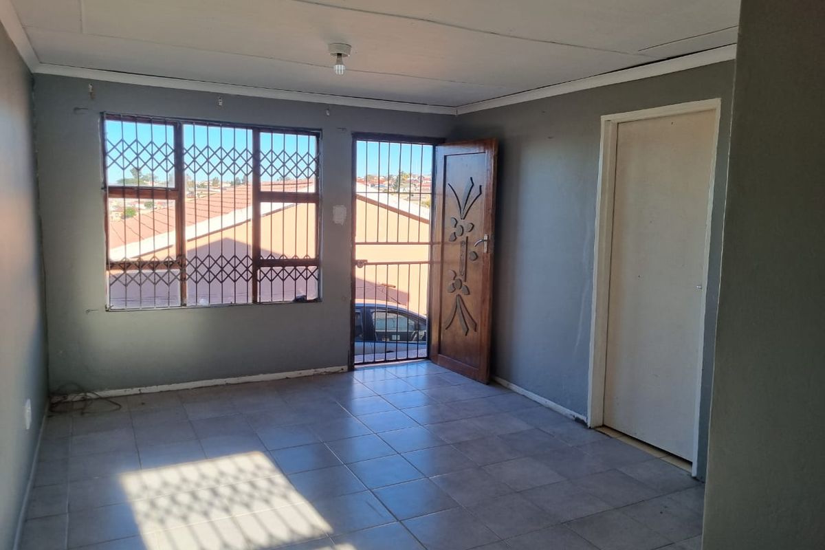 An empty living room featuring tiled flooring, security gates on windows and doors, and neutral grey walls, offering a blank canvas for interior design.