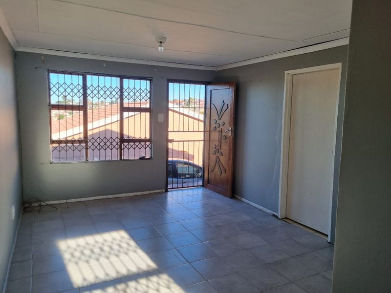 An empty living room featuring tiled flooring, security gates on windows and doors, and neutral grey walls, offering a blank canvas for interior design.