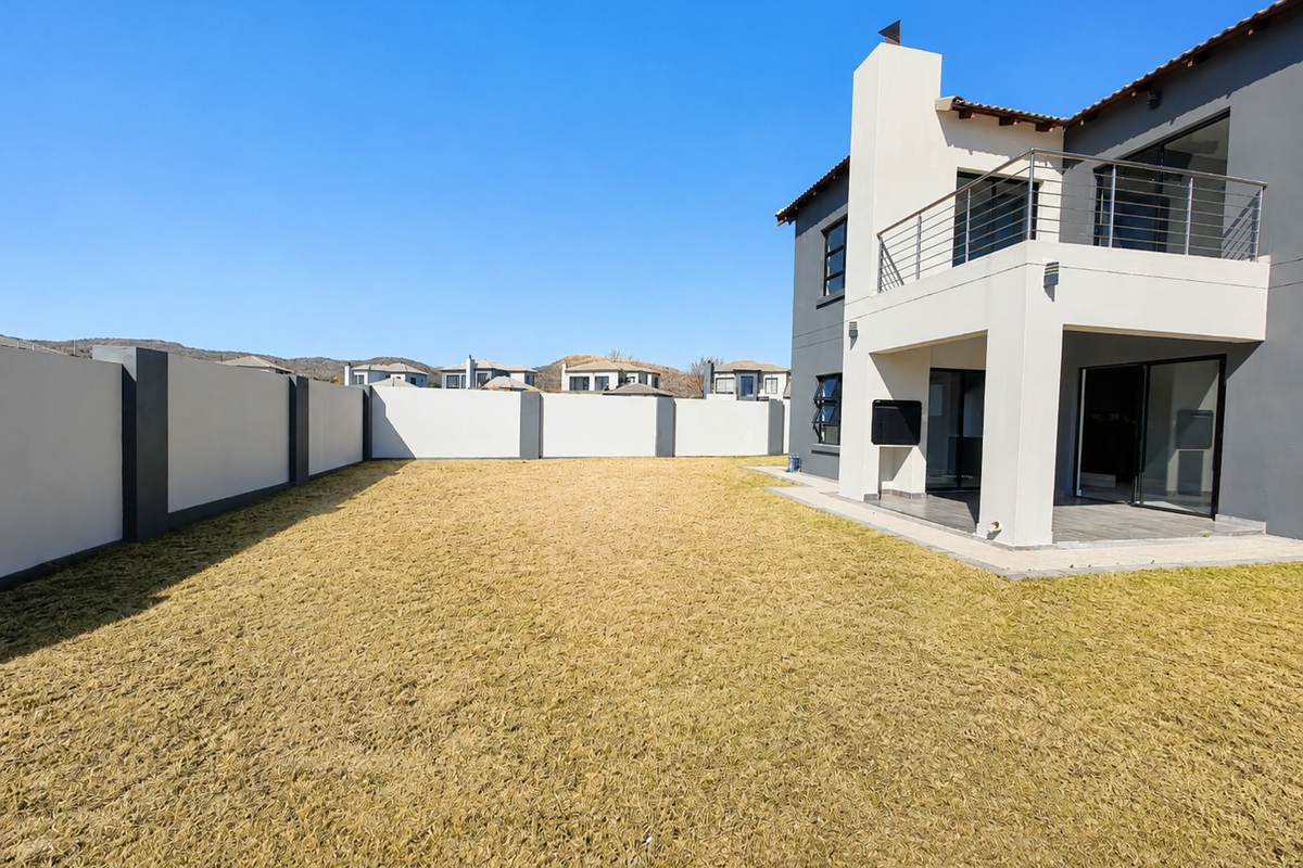 Spacious rear garden with a perimeter wall, featuring a covered patio with a built-in braai and an upper-level balcony with stainless steel balustrades.