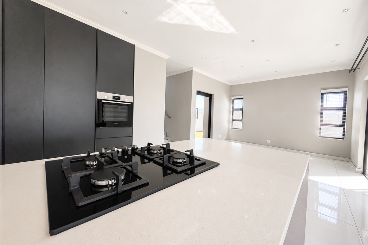 Modern kitchen featuring a large stone island with a built-in gas hob, sleek dark cabinetry, integrated oven, and bright tiled flooring.
