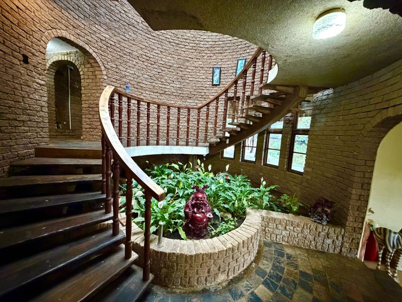 A unique architectural entrance hall featuring curved brick walls, a central internal garden planter, and a sweeping timber staircase.
