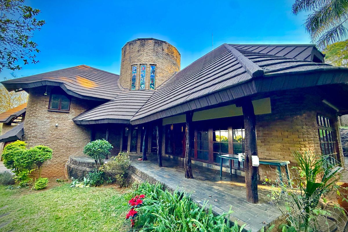 A unique architectural rear elevation featuring a distinctive brick tower, stained glass windows, and a covered patio area with timber supports overlooking the garden.
