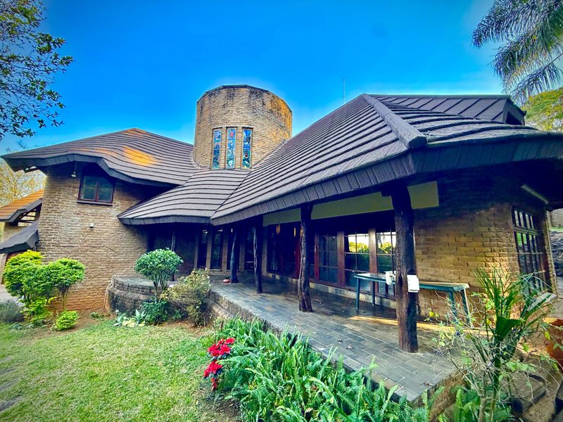 A unique architectural rear elevation featuring a distinctive brick tower, stained glass windows, and a covered patio area with timber supports overlooking the garden.