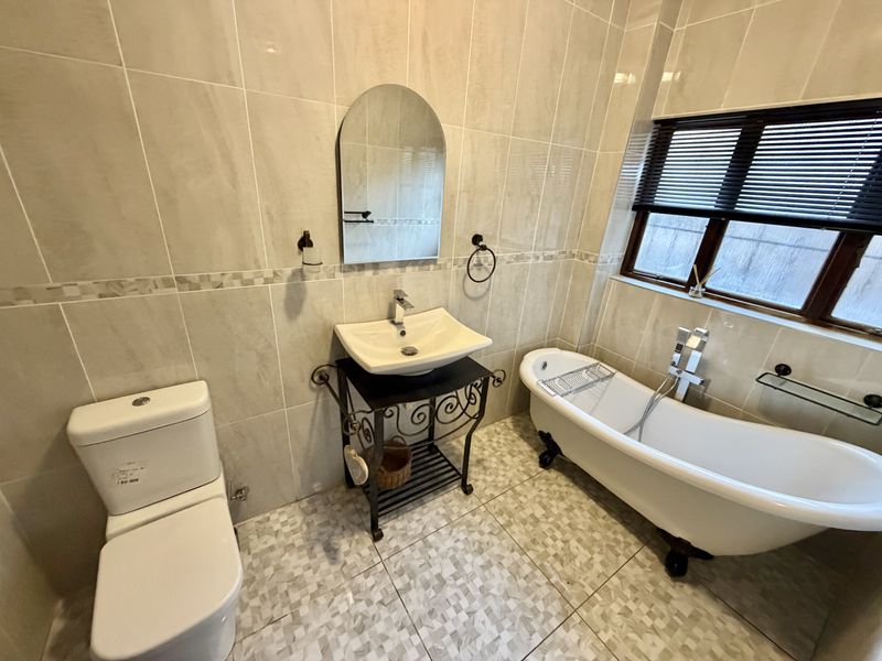 A well-maintained bathroom featuring a classic freestanding bathtub, a modern vessel sink vanity, and neutral floor-to-ceiling wall tiling.