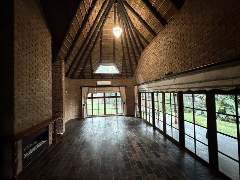 Spacious living area featuring a high vaulted thatched ceiling, exposed brick walls, a built-in fireplace, and large glass doors opening to the garden.