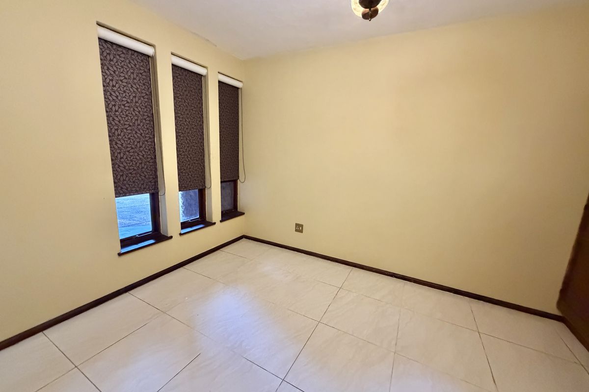 An empty bedroom featuring tiled flooring, neutral walls, and three windows fitted with dark roller blinds.