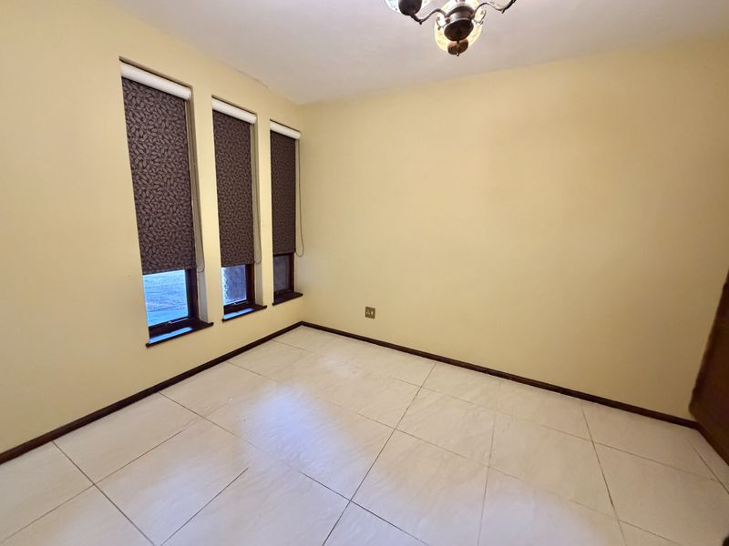 An empty bedroom featuring tiled flooring, neutral walls, and three windows fitted with dark roller blinds.
