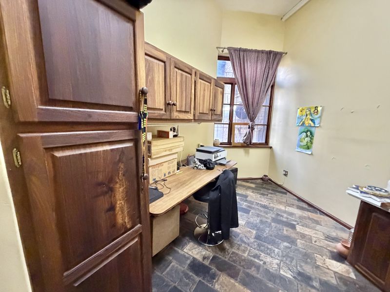 A home office featuring built-in wooden cabinetry, a fitted desk, and durable stone tile flooring, offering a functional workspace with natural light.