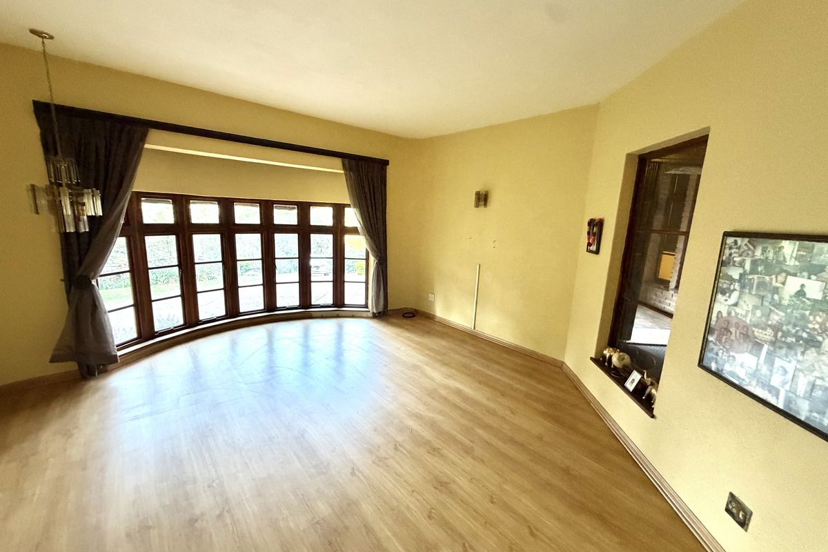 A spacious, empty living room featuring large bay windows, laminate flooring, and neutral wall tones, offering a bright and versatile living space.
