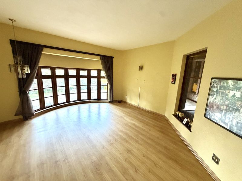 A spacious, empty living room featuring large bay windows, laminate flooring, and neutral wall tones, offering a bright and versatile living space.