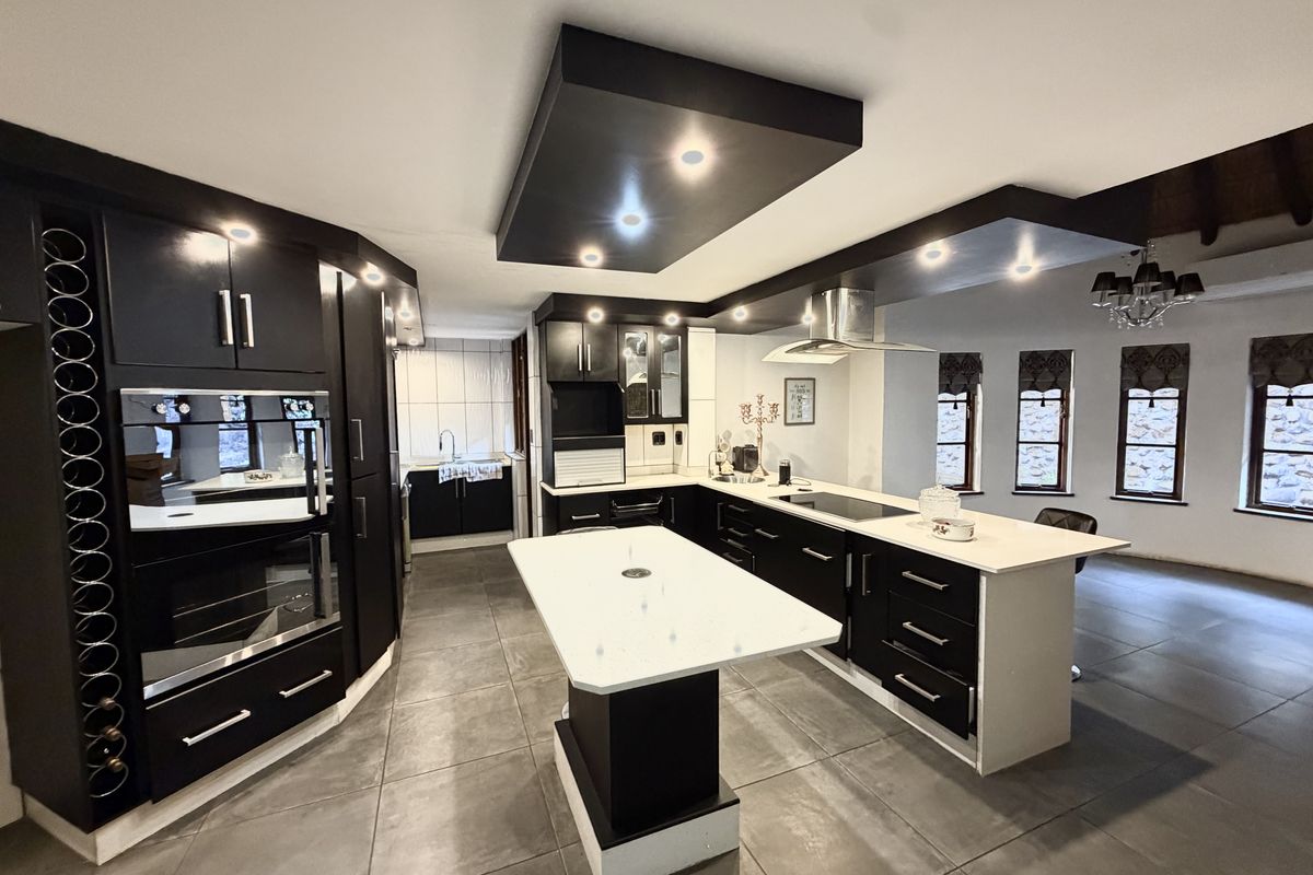 Modern kitchen featuring dark cabinetry, stone countertops, a central island, built-in appliances, and recessed ceiling lighting with large format floor tiles.