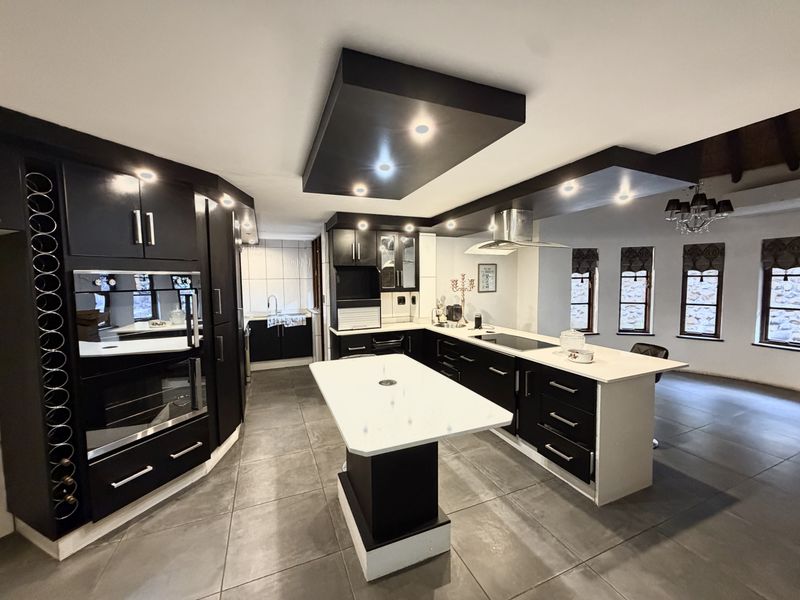Modern kitchen featuring dark cabinetry, stone countertops, a central island, built-in appliances, and recessed ceiling lighting with large format floor tiles.