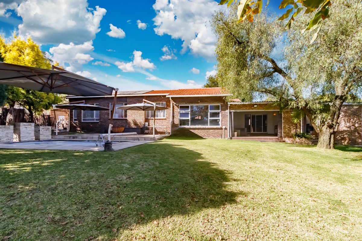 Spacious rear exterior featuring a brick facade, covered patio, swimming pool, and a large, well-maintained garden area.
