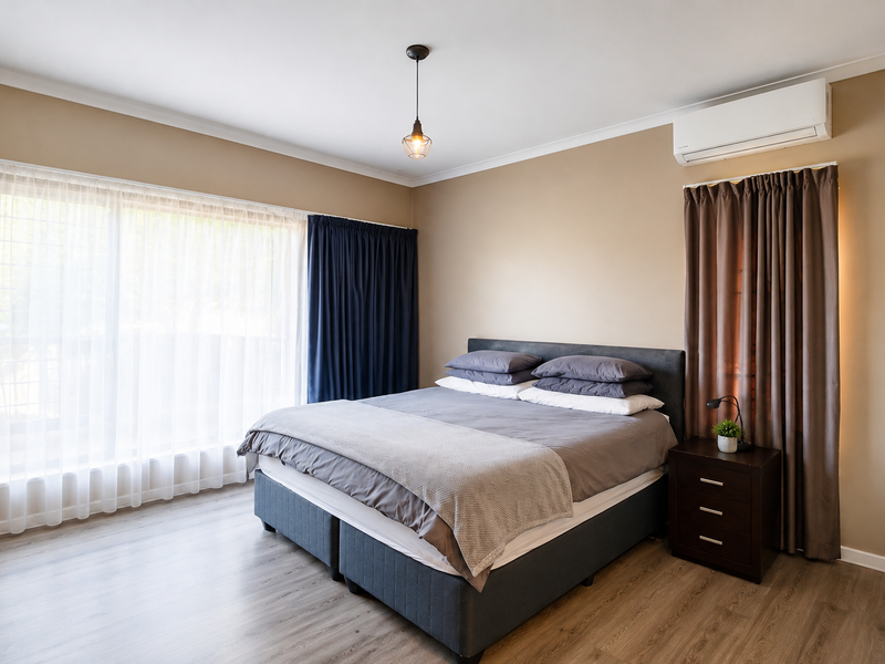 A well-maintained bedroom featuring laminate flooring, a wall-mounted split-system air conditioner, and neutral wall tones with large windows for natural light.