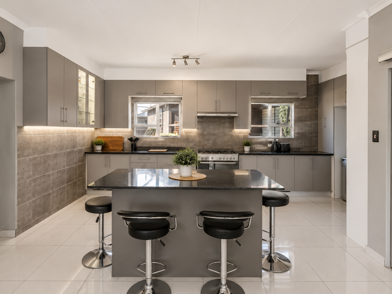 Modern kitchen featuring a central island with granite countertops, sleek grey cabinetry, gas hob, extractor fan, and contemporary tiled finishes.