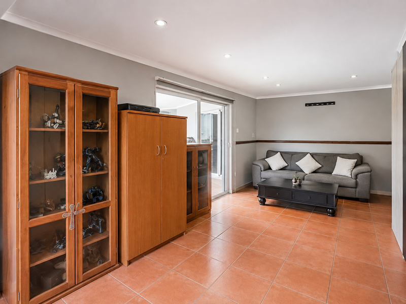 A spacious living room featuring tiled flooring, recessed downlighting, and a sliding glass door providing access to the outdoor area.