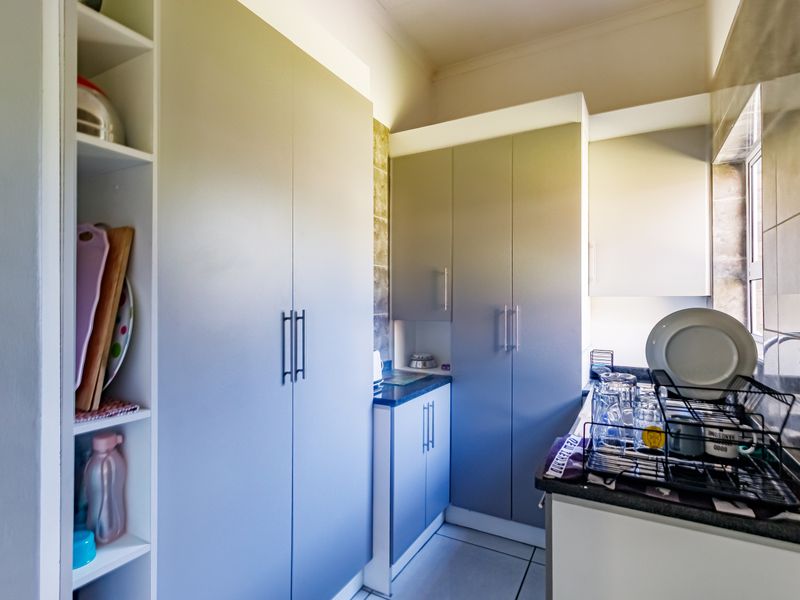 A functional scullery area featuring modern grey built-in cabinetry, laminate countertops, and tiled splashbacks, providing additional storage and prep space.