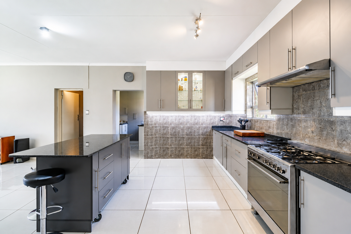 Modern kitchen featuring granite countertops, a gas stove with extractor, ample built-in cabinetry, and a functional central island with tiled flooring throughout.