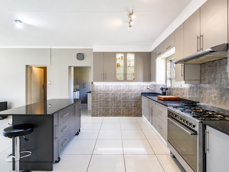 Modern kitchen featuring granite countertops, a gas stove with extractor, ample built-in cabinetry, and a functional central island with tiled flooring throughout.