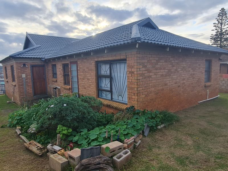 Rear view of a face brick house featuring a tiled roof, security bars on windows, and a surrounding garden with concrete block boundary walls.