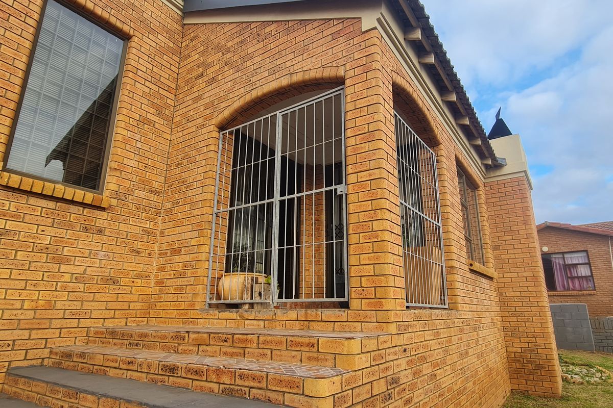 A rear exterior view of a face brick house featuring a tiled patio area enclosed with security gates and aluminium window frames.