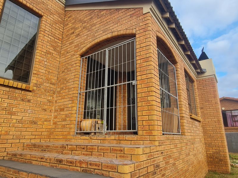 A rear exterior view of a face brick house featuring a tiled patio area enclosed with security gates and aluminium window frames.
