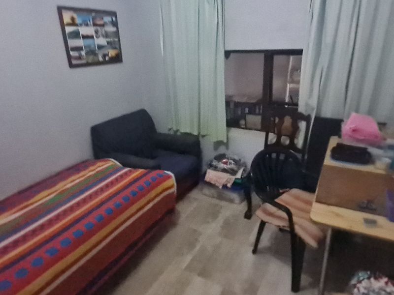 A compact bedroom featuring tiled flooring and a window with curtains, offering a functional space for rest or study.