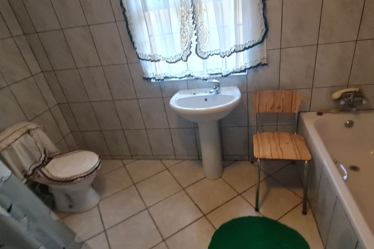 A functional bathroom featuring a pedestal basin, bathtub, and toilet with full-height wall tiling and tiled flooring.