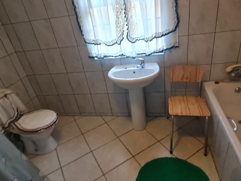 A functional bathroom featuring a pedestal basin, bathtub, and toilet with full-height wall tiling and tiled flooring.