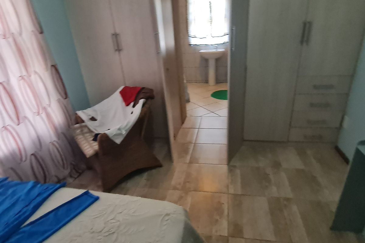 A bedroom featuring built-in cupboards and tiled flooring, with an adjoining en-suite bathroom area visible through the doorway.