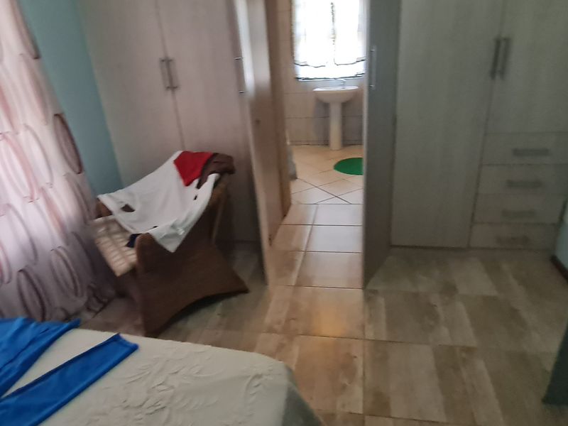 A bedroom featuring built-in cupboards and tiled flooring, with an adjoining en-suite bathroom area visible through the doorway.