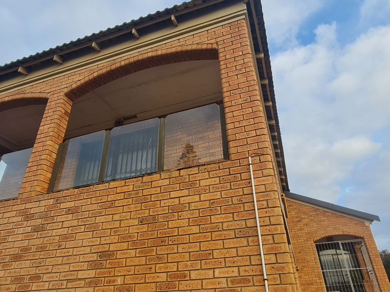 A view of the rear exterior featuring a face brick facade, an arched balcony with a modern glass balustrade, and a tiled roof.
