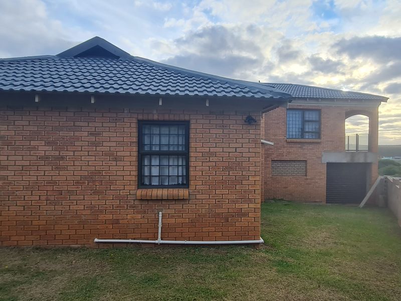 Rear view of a face brick house featuring a tiled roof, security-barred windows, and a concrete boundary wall in a residential setting.