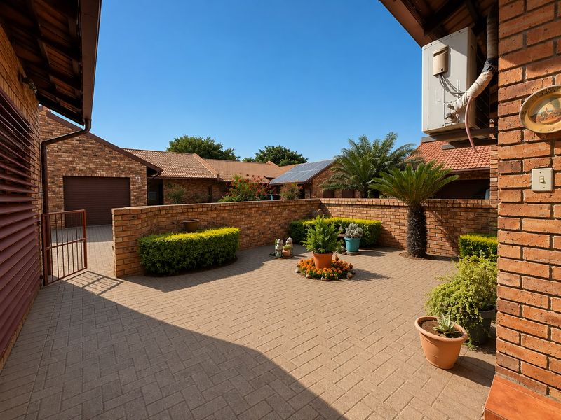 A well-maintained paved front courtyard featuring face brick walls, established landscaping, and access to a garage, set within a neat townhouse complex.