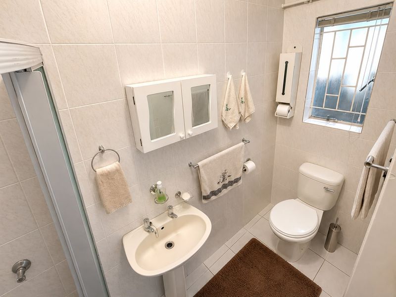 A functional bathroom featuring a pedestal basin, toilet, and wall-mounted medicine cabinet, finished with neutral wall and floor tiles.