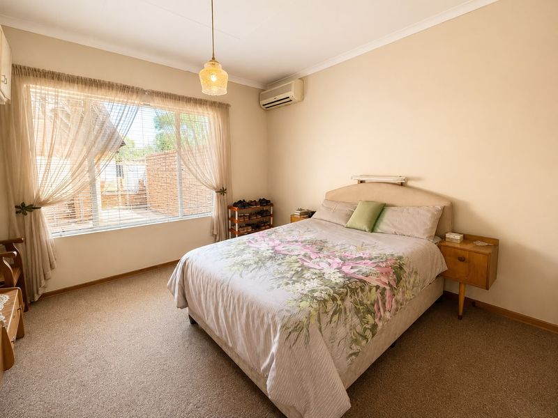 A well-lit bedroom featuring neutral walls, carpeted flooring, a split-system air conditioner, and a large window with natural light.