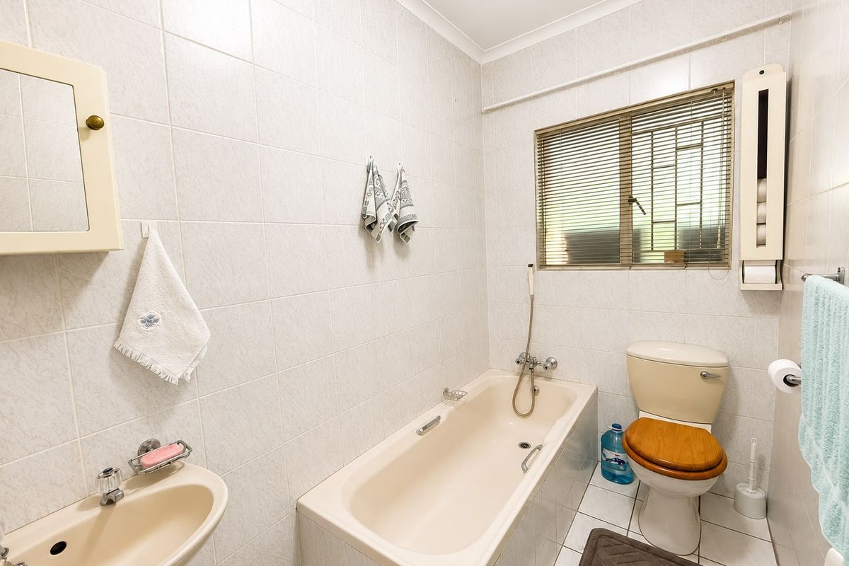 A functional bathroom featuring a bathtub, toilet, and wall-mounted basin with full-height wall tiling and a window for natural light.