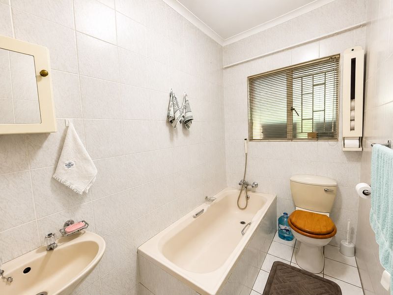 A functional bathroom featuring a bathtub, toilet, and wall-mounted basin with full-height wall tiling and a window for natural light.