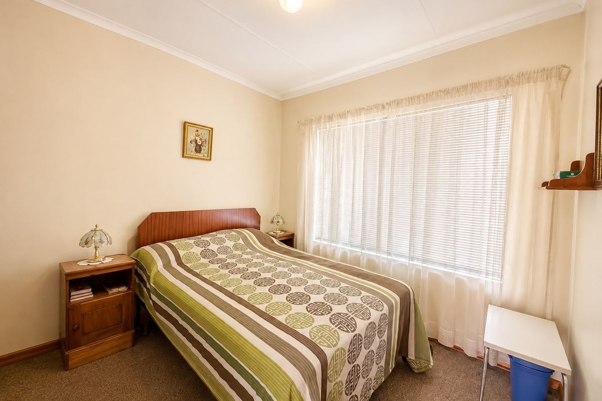 A functional bedroom featuring neutral wall finishes, carpeted flooring, and venetian blinds, offering a clean and simple space ready for personalization.