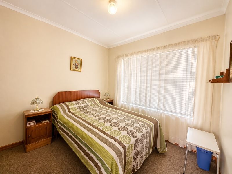 A functional bedroom featuring neutral wall finishes, carpeted flooring, and venetian blinds, offering a clean and simple space ready for personalization.