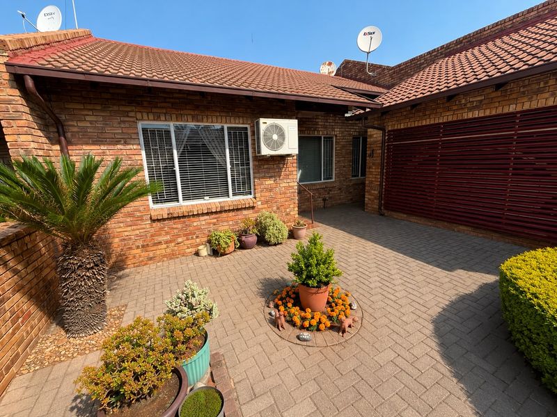 A well-maintained townhouse front entrance featuring a paved courtyard, face brick exterior, and integrated air conditioning unit.