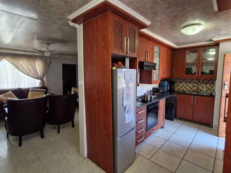 Open-plan kitchen and living area featuring wood-finish cabinetry, tiled flooring, and integrated kitchen appliances, creating a functional and connected living space.