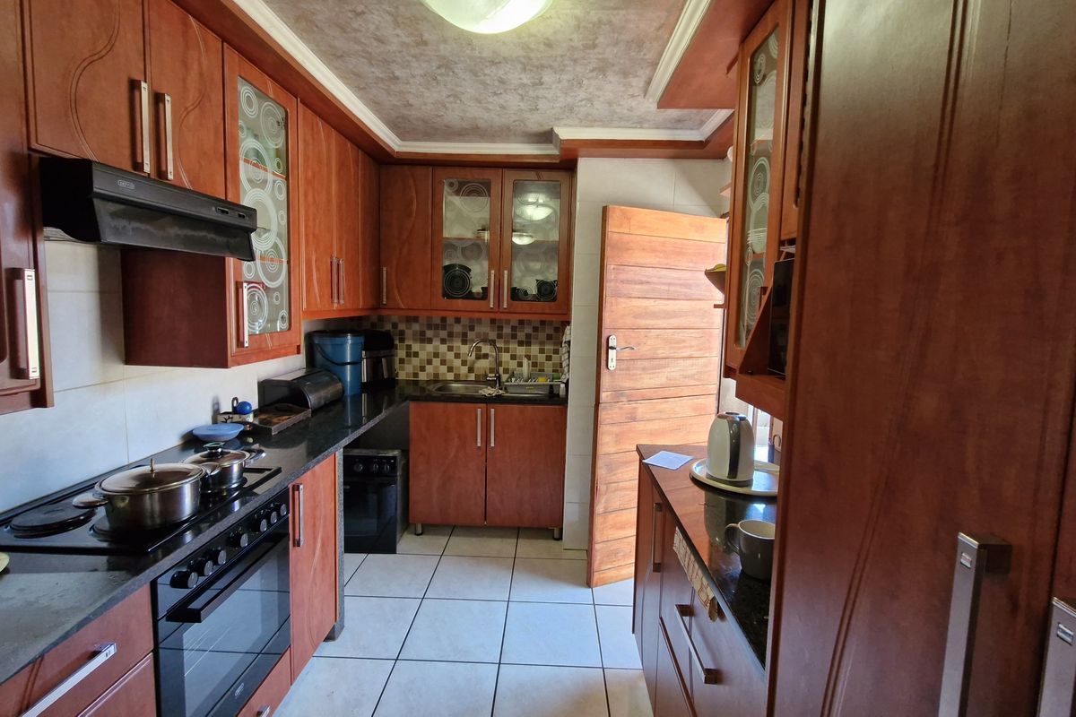 A functional kitchen featuring warm-toned wooden cabinetry, granite countertops, a built-in oven with hob, and tiled flooring with direct access to the exterior.