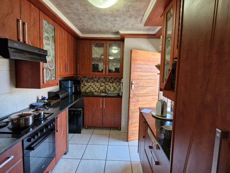 A functional kitchen featuring warm-toned wooden cabinetry, granite countertops, a built-in oven with hob, and tiled flooring with direct access to the exterior.
