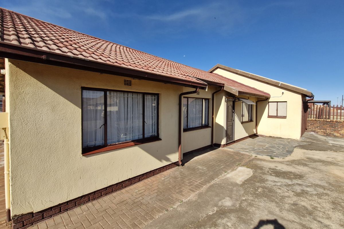 Rear view of the house featuring a paved patio area, terracotta tiled roof, and concrete driveway with established boundary walling.