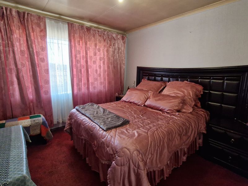 A bedroom featuring a built-in headboard, red carpeting, and window curtains.